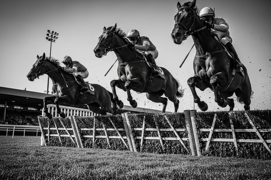 Racehorses clearing a hurdle at full stretch